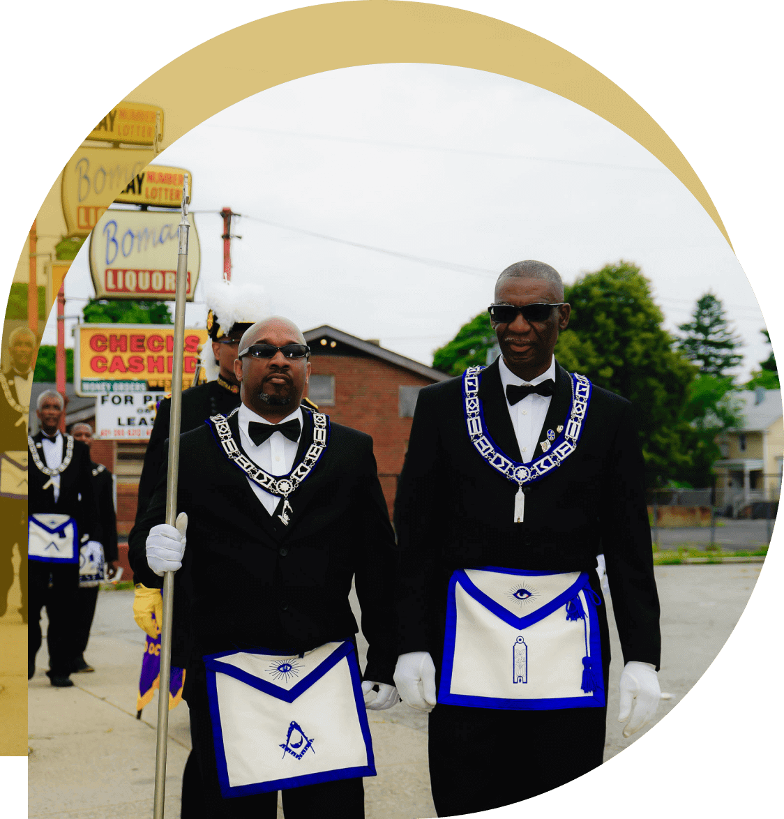 Two men in suits and white gloves are walking down the street.
